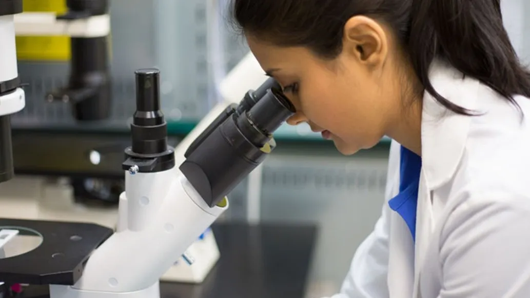 Technicienne observant un échantillon au microscope dans un laboratoire de contrôle qualité